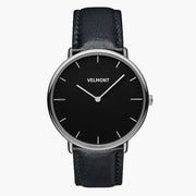 Watch with a black dial and silver-tone case on a black strap, shown from the front.