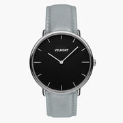 A black dial framed by a slim silver-tone case, set on a dove gray strap.