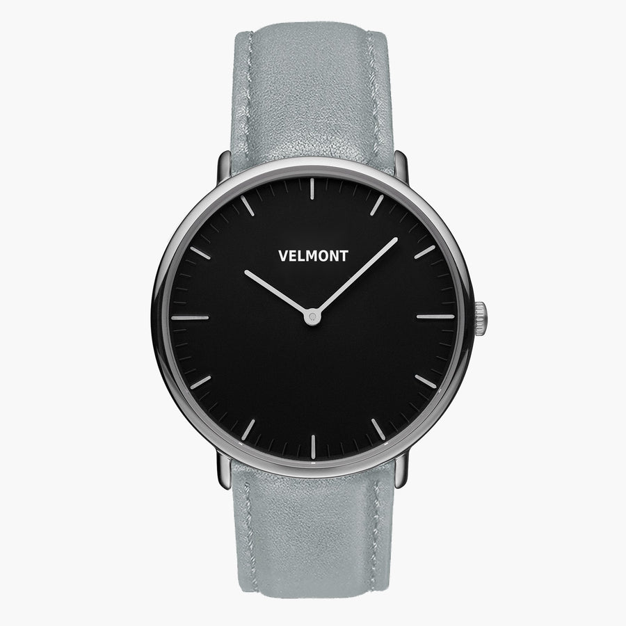 A black dial framed by a slim silver-tone case, set on a dove gray strap.