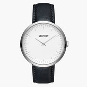 Minimalist watch with a white dial and silver-tone case on a black strap.