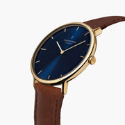 Watch turned at an angle, blue sunburst dial and gold-tone bezel catching the light.