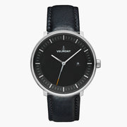 Watch with a black dial and silver-tone case on a black strap, shown from the front.