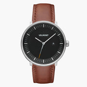 Watch with a black dial and silver-tone case on a brown strap, shown from the front.