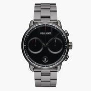 Chronograph-style watch with a black dial on a gunmetal link bracelet, front view.
