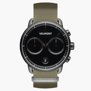 Chronograph-style watch with a black dial and gunmetal case on an olive woven strap.