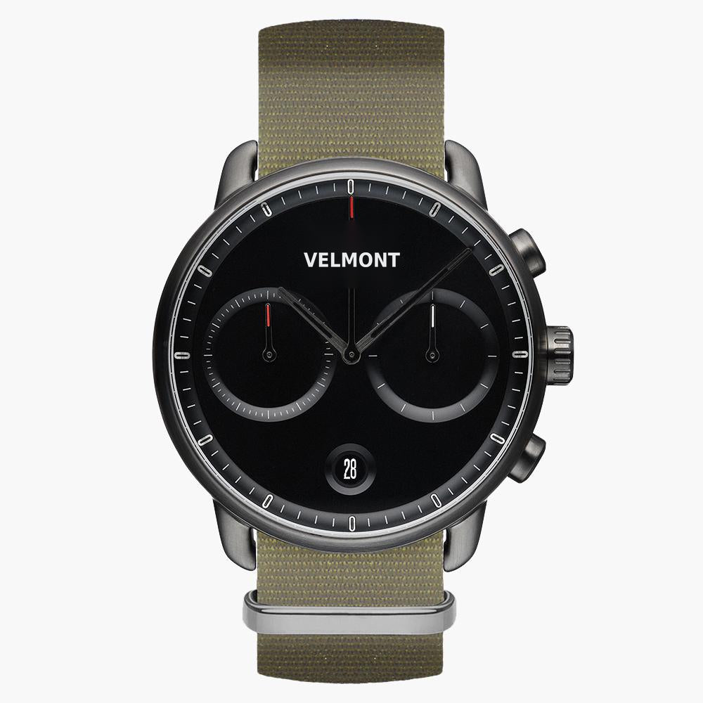 Chronograph-style watch with a black dial and gunmetal case on an olive woven strap.