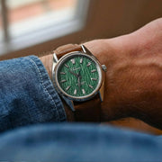 Green-dial watch on the wrist with a denim cuff