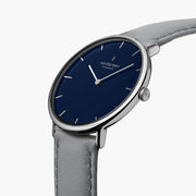 Three-quarter view of the thin silver-tone case and blue dial on a gray strap.