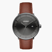 Watch with a dark gray sunburst dial and gunmetal case on a brown strap.