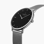 Watch turned at an angle, black dial and silver-tone bezel catching the light.