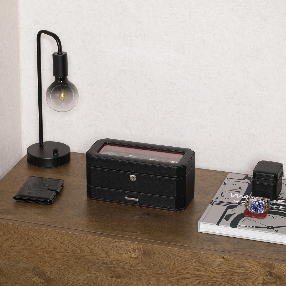 Closed black watch box on a wooden desk beside a lamp
