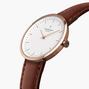Angled view of the slim rose gold-tone case and crown on a brown strap.
