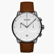 Chronograph-style watch with a white dial and gunmetal case on a brown strap.