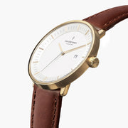 Watch turned at an angle, white dial and gold-tone bezel catching the light.