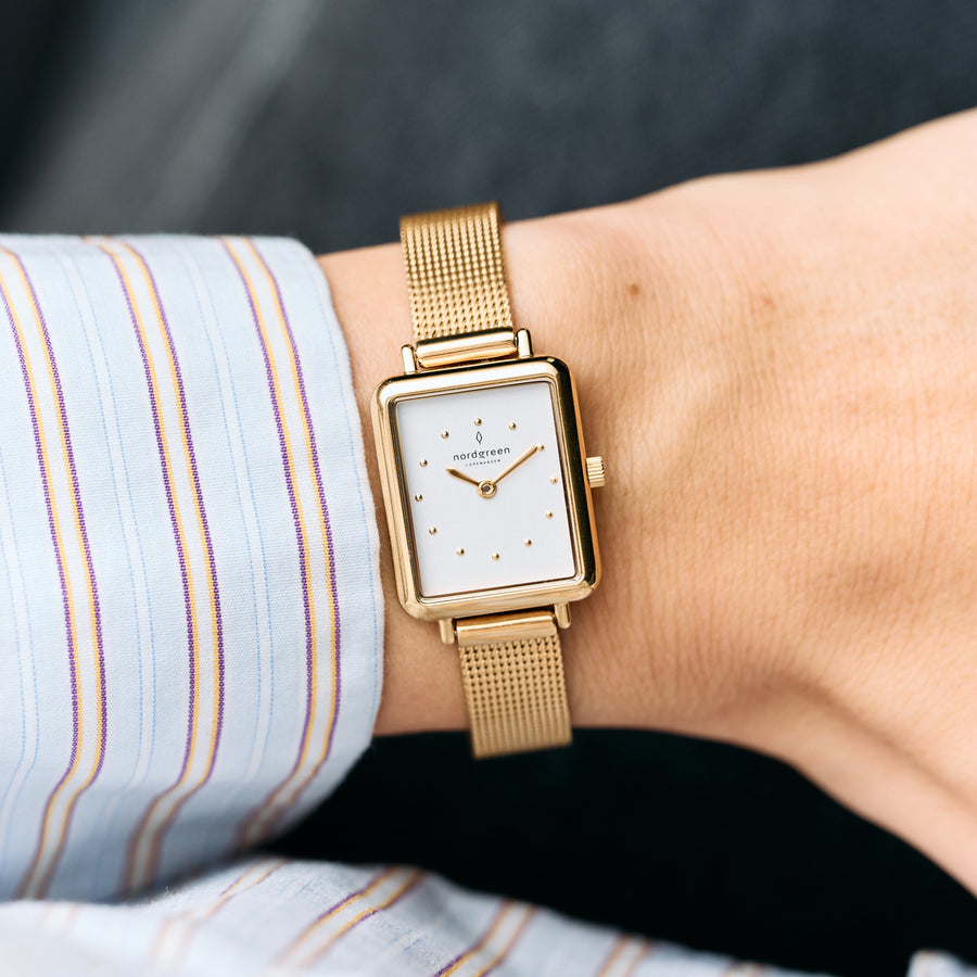 Rectangular watch with a white dial worn with a striped shirt cuff.