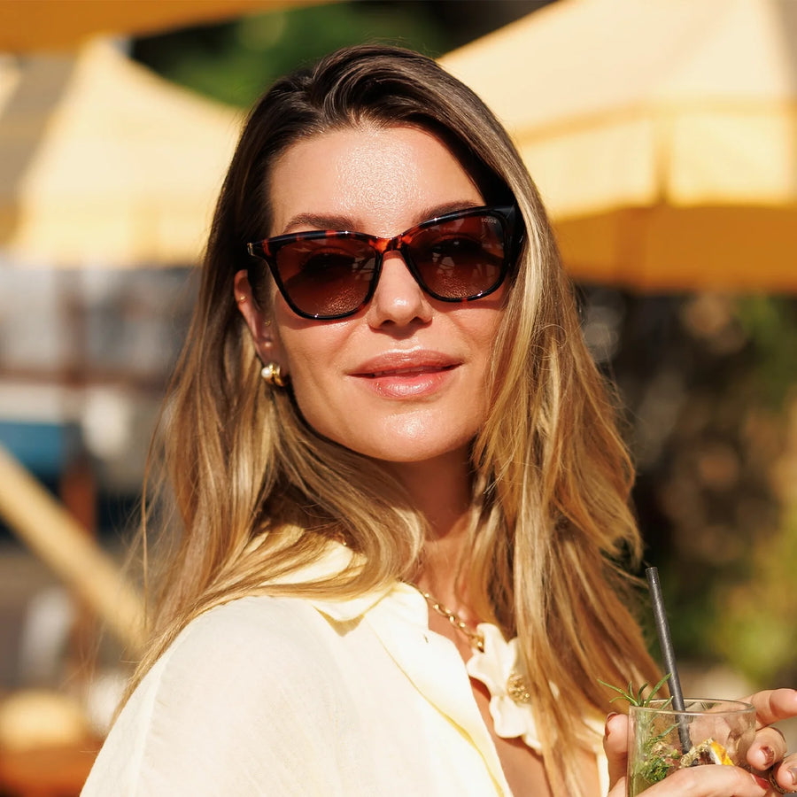 Woman in tortoise cat eye sunglasses holding a drink