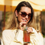Woman smiling in cat eye sunglasses with a drink