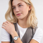 Woman in a white tee and gray vest wearing the silver-tone watch.