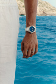 Hand by the water wearing the blue-dial watch