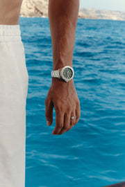 Watch with green dial worn on the wrist above the sea