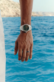 Hand by the water wearing the green-dial watch
