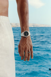 Hand by the water wearing the black-dial watch