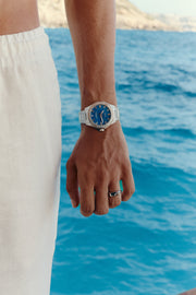 Watch with blue dial worn on the wrist above the sea