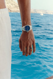 Hand by the water wearing the blue-dial watch