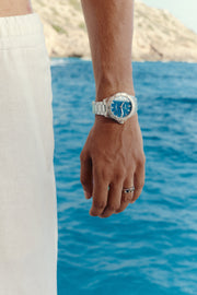 Watch with blue dial worn on the wrist above the sea