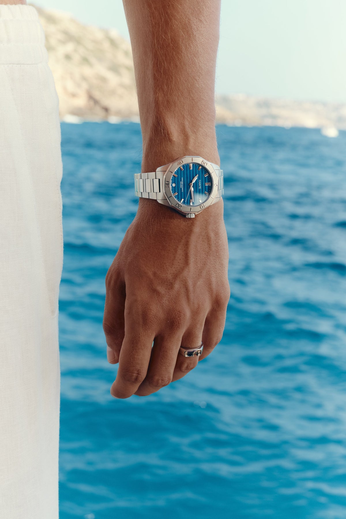 Hand by the water wearing the blue-dial watch