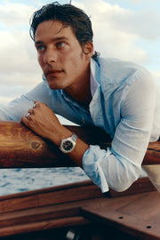 Man in a linen shirt leaning on a boat rail wearing the watch