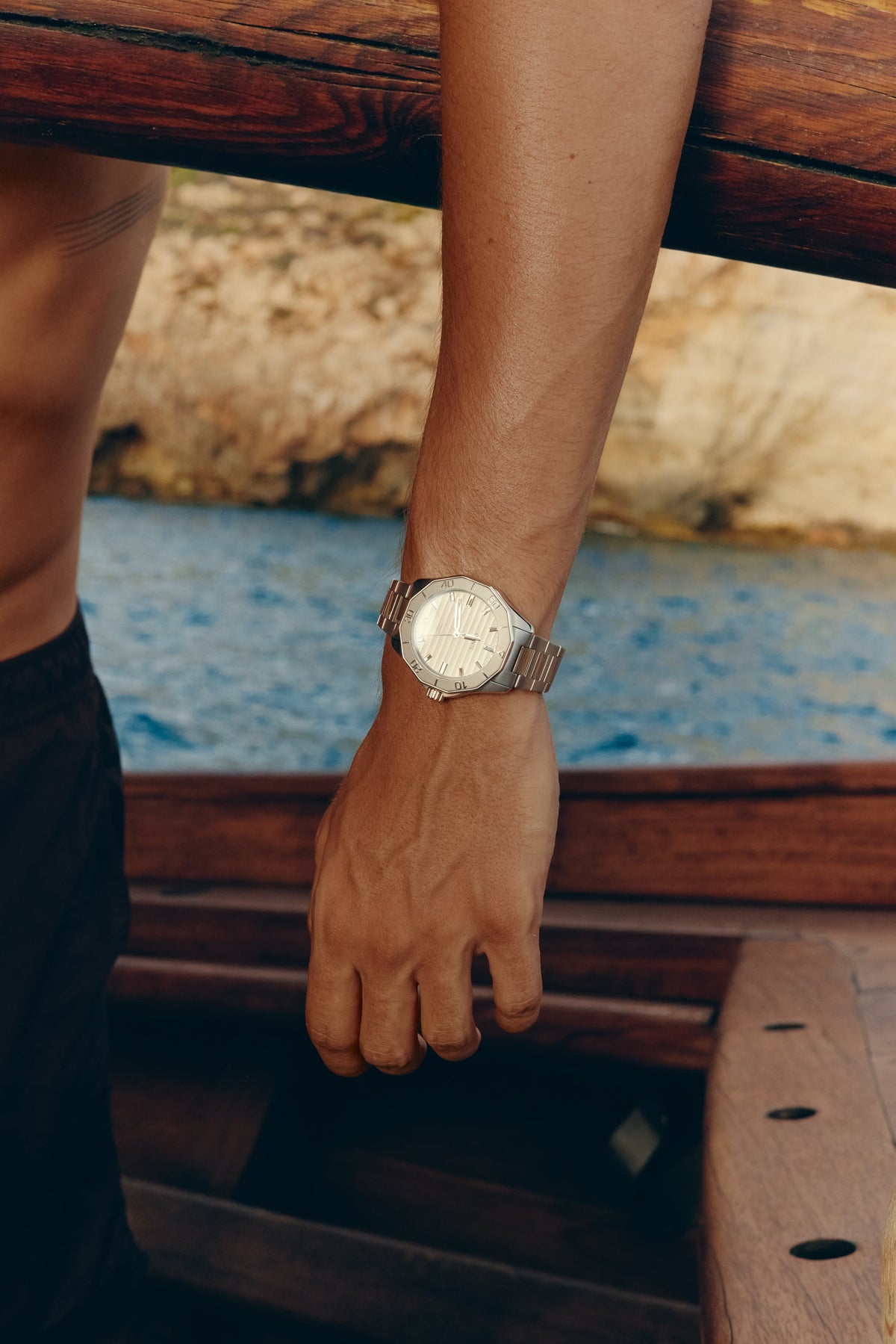 Hand on the wooden edge of a boat wearing the watch