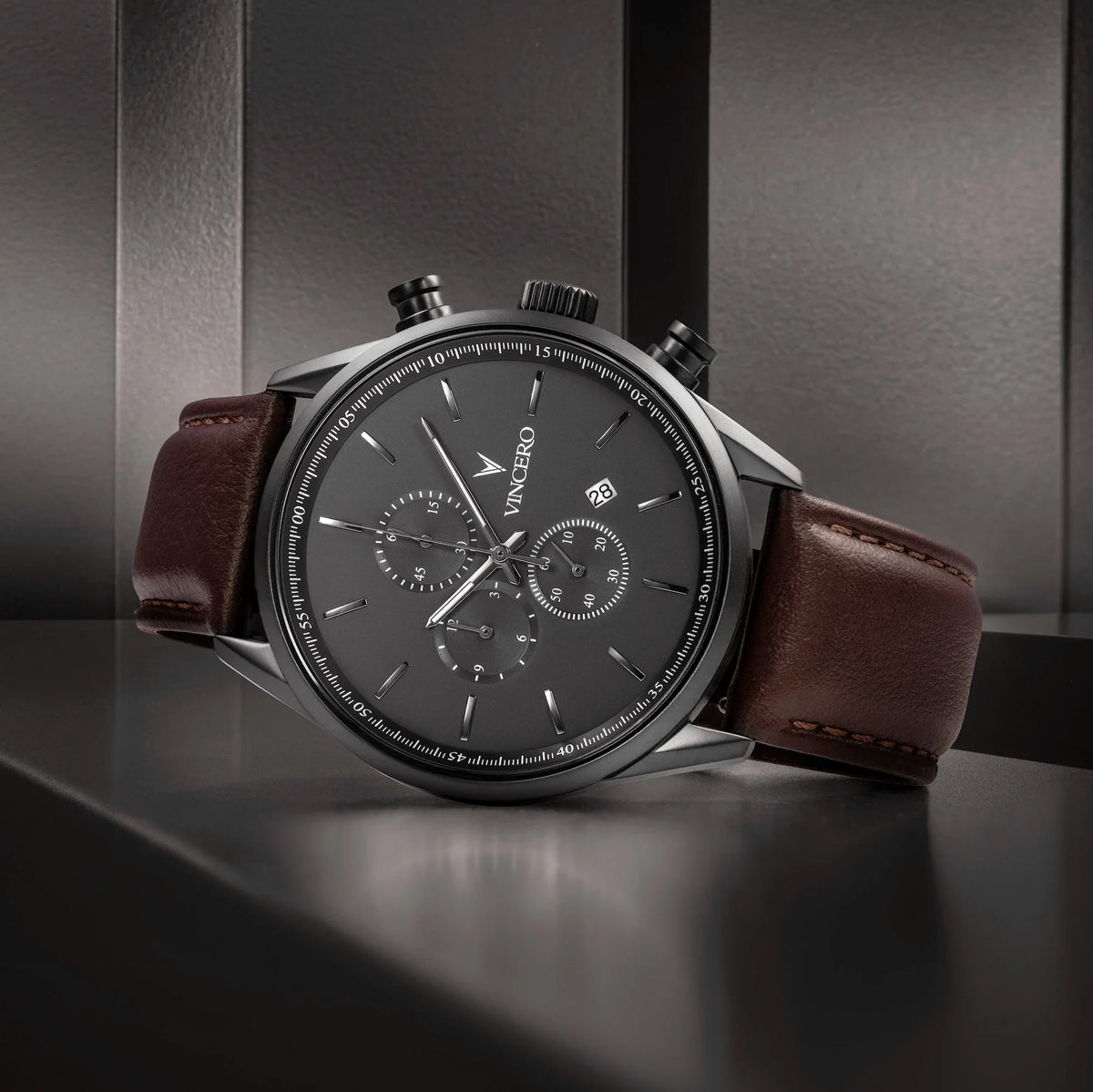 Gunmetal chronograph on a dark shelf, angled view