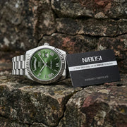 Green dial watch on a rock with a card