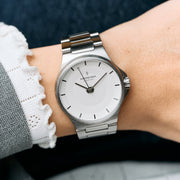 The silver-tone watch worn on a wrist with a white lace cuff and gray coat.