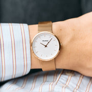 The rose gold-tone watch worn on a wrist with a striped shirt cuff.