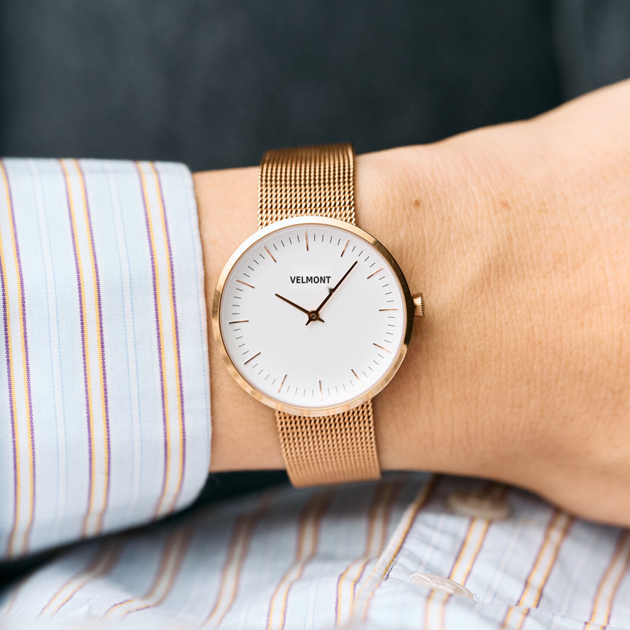 The rose gold-tone watch worn on a wrist with a striped shirt cuff.
