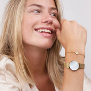Smiling woman wearing the small gold-tone watch with a delicate chain bracelet.