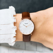 Worn on a wrist with a white ruffled cuff, brown strap and rose gold-tone case.