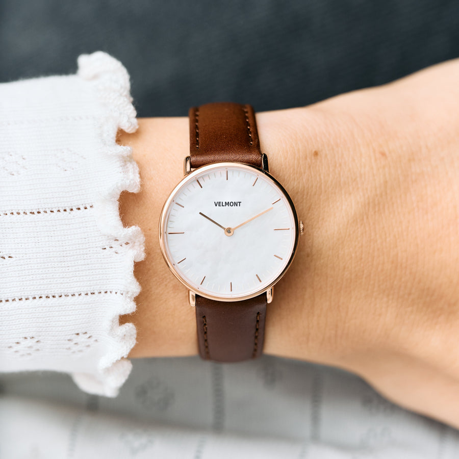 Worn on a wrist with a white ruffled cuff, brown strap and rose gold-tone case.