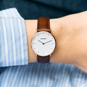 Small white-dial watch worn with a blue striped shirt and brown strap.