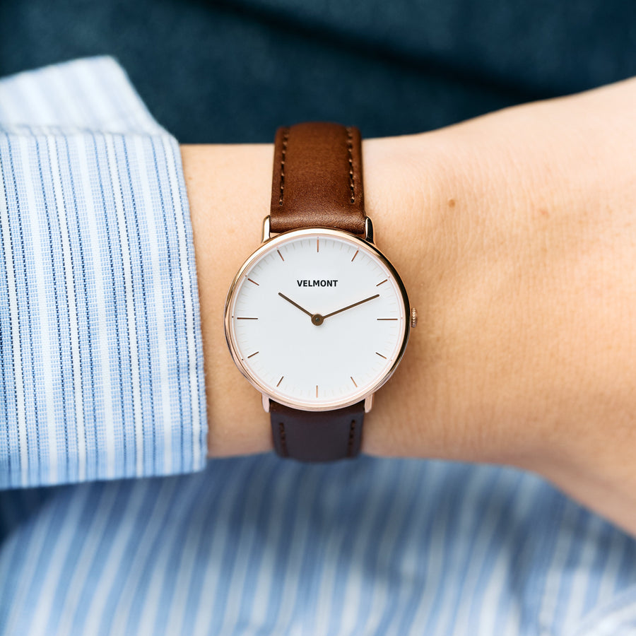 Small white-dial watch worn with a blue striped shirt and brown strap.