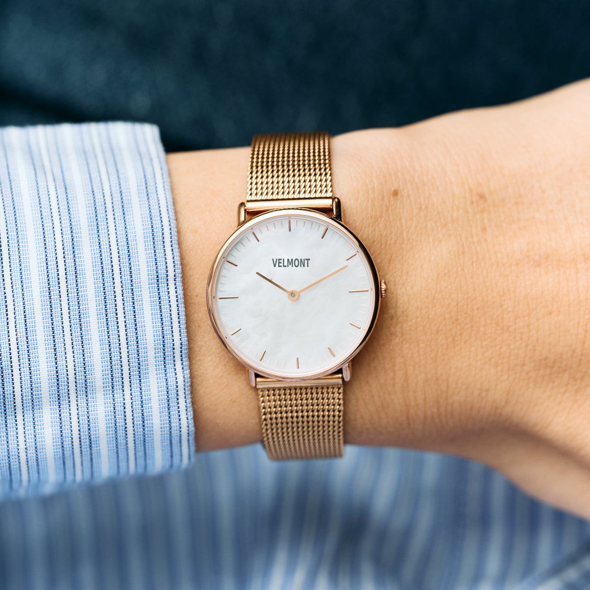 The pearlescent-dial watch on a wrist, paired with a blue striped shirt cuff.