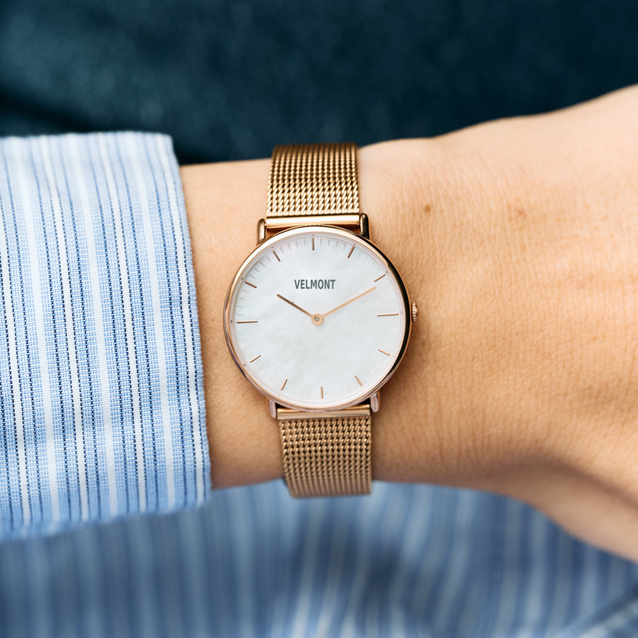 The pearlescent-dial watch on a wrist, paired with a blue striped shirt cuff.