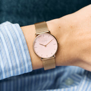 The watch worn on a wrist with a blue striped shirt cuff.