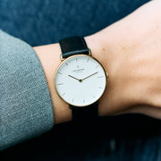 The watch worn on a wrist beside a gray herringbone jacket sleeve.