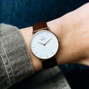 Rose gold-tone watch on a wrist beside a herringbone sleeve, dark brown strap.