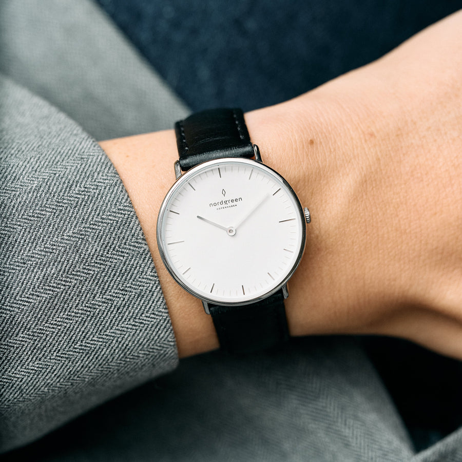 Worn on the wrist with a gray herringbone blazer, white dial and black strap.