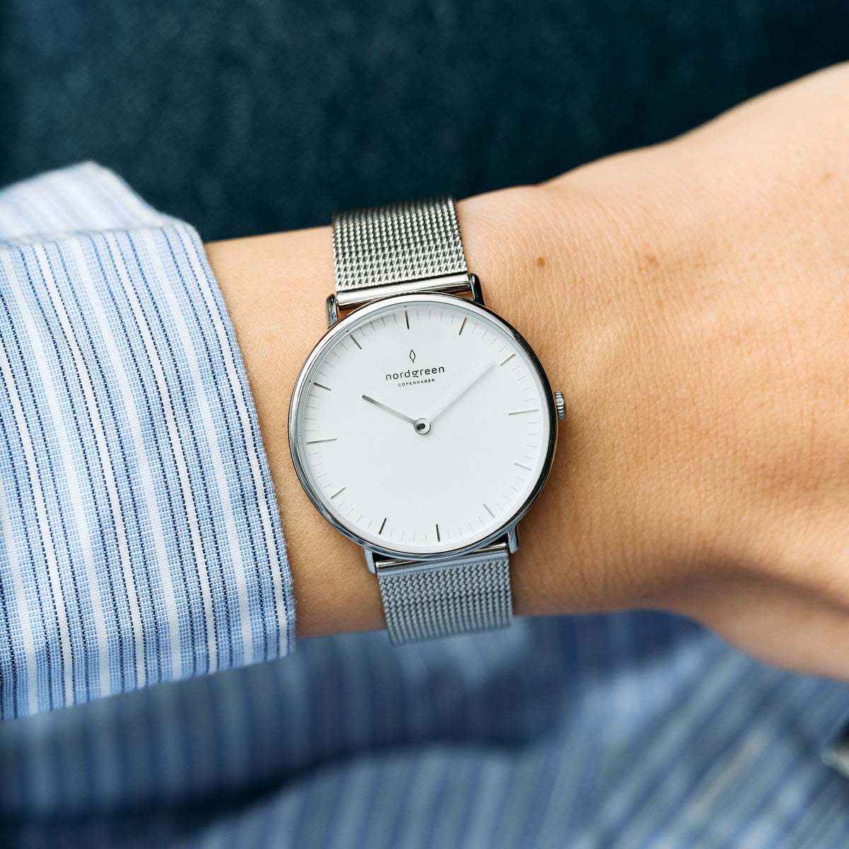 Mesh-strap watch worn with a blue striped shirt, seen from above.