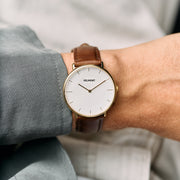 Gold-tone watch on a wrist next to a gray-green shirt sleeve.